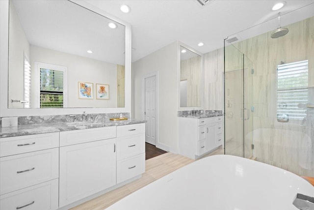 full bathroom featuring recessed lighting, vanity, a shower stall, wood finished floors, and a freestanding tub