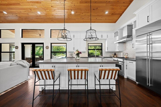 kitchen featuring high end appliances, pendant lighting, white cabinetry, and wall chimney exhaust hood