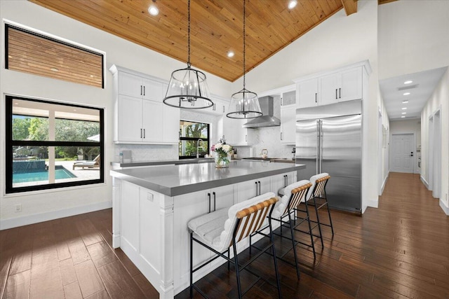 kitchen featuring built in fridge, a center island, pendant lighting, white cabinetry, and wall chimney exhaust hood