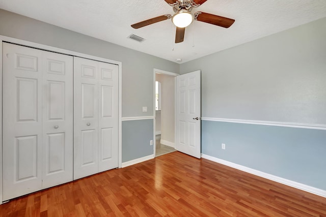 unfurnished bedroom with wood-type flooring, a textured ceiling, ceiling fan, and a closet