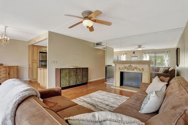 living room with ceiling fan with notable chandelier, light hardwood / wood-style flooring, and a textured ceiling