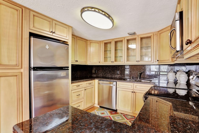 kitchen featuring sink, backsplash, stainless steel appliances, light brown cabinetry, and dark stone counters