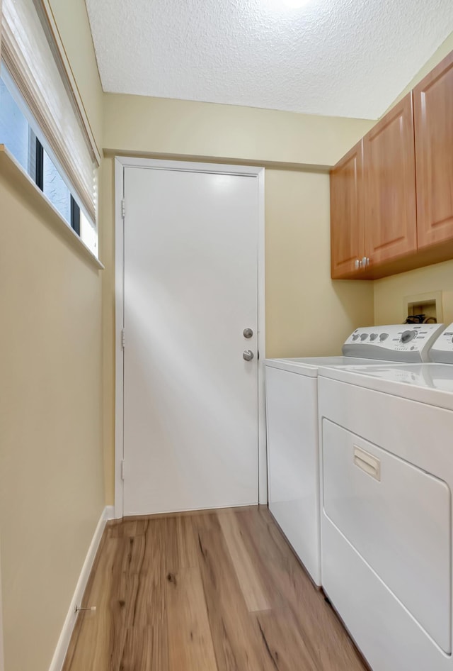 washroom with cabinets, washer and dryer, a textured ceiling, and light hardwood / wood-style floors