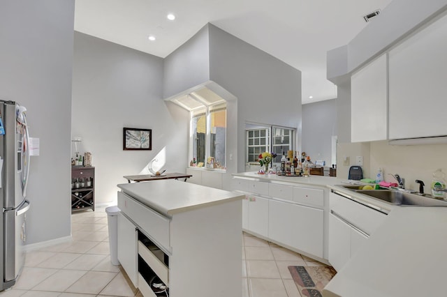 kitchen featuring light tile patterned flooring, sink, white cabinetry, stainless steel fridge, and a kitchen island