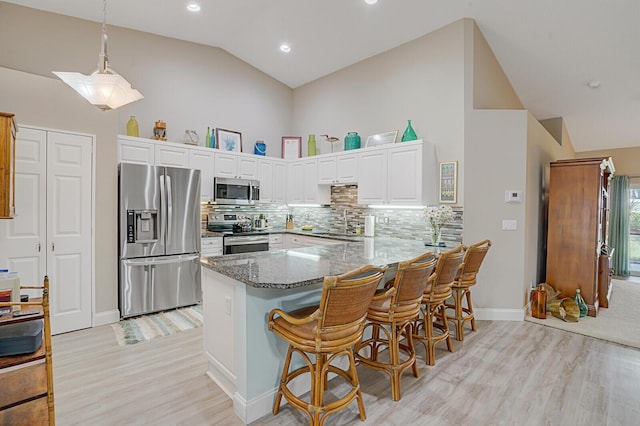 kitchen featuring pendant lighting, appliances with stainless steel finishes, white cabinetry, kitchen peninsula, and dark stone counters