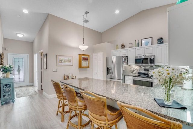 kitchen with light wood-style flooring, a peninsula, high vaulted ceiling, stainless steel appliances, and white cabinetry