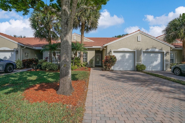 ranch-style home with a tiled roof, decorative driveway, an attached garage, and stucco siding