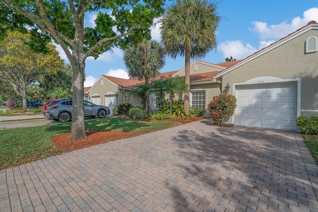 view of front of property with an attached garage, a tiled roof, decorative driveway, and stucco siding