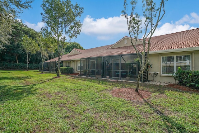 rear view of property featuring a sunroom, a tiled roof, stucco siding, and a yard