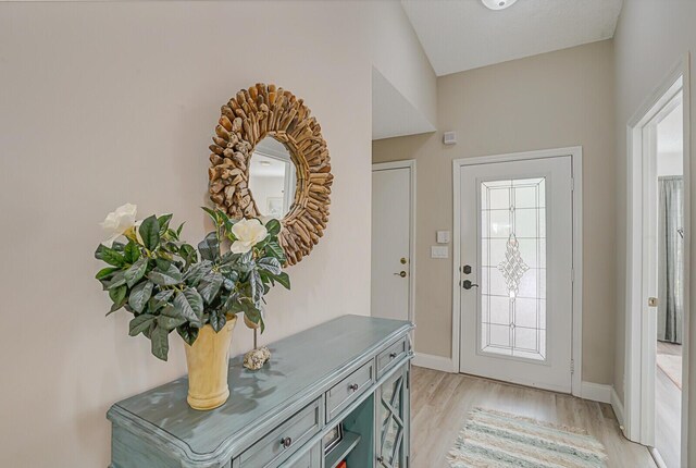 foyer entrance featuring lofted ceiling, light wood finished floors, and baseboards