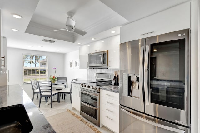 kitchen featuring white cabinetry, a tray ceiling, light stone countertops, and appliances with stainless steel finishes