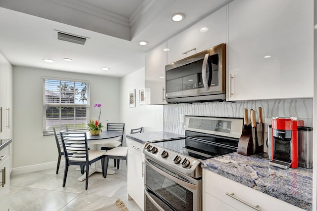 kitchen with appliances with stainless steel finishes, white cabinetry, stone countertops, decorative backsplash, and light tile patterned flooring