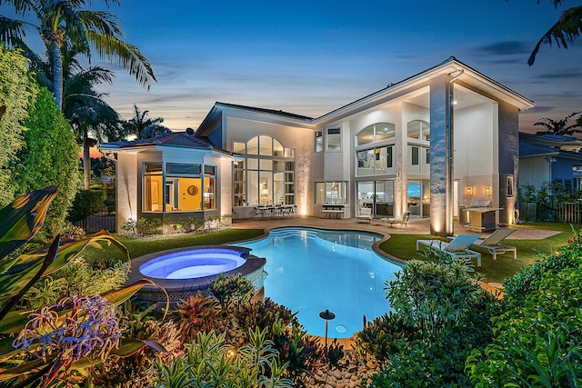 pool at dusk featuring an in ground hot tub and a patio area