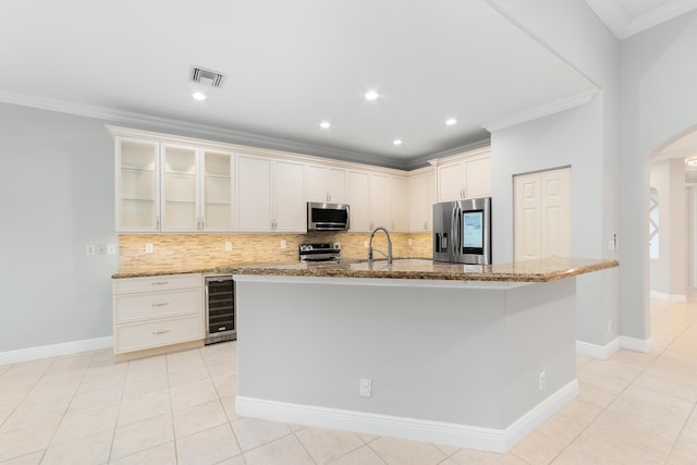 kitchen with light stone counters, appliances with stainless steel finishes, a center island with sink, and wine cooler