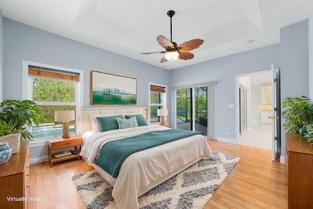 bedroom featuring access to exterior, a raised ceiling, and light hardwood / wood-style floors