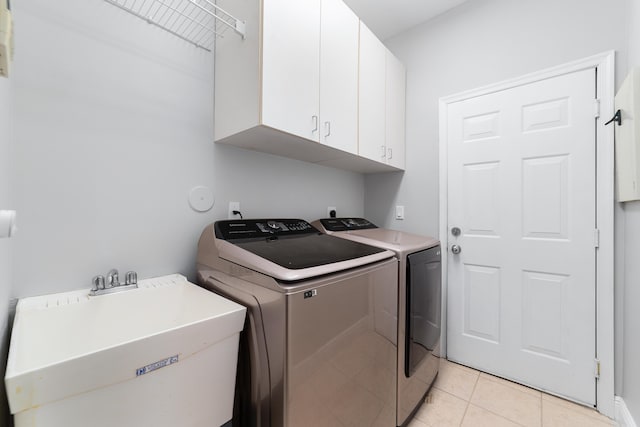 clothes washing area with sink, light tile patterned floors, washer and clothes dryer, and cabinets