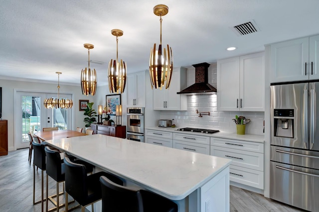 kitchen featuring visible vents, stainless steel appliances, wall chimney range hood, and white cabinetry