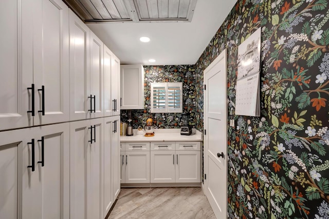 kitchen featuring wallpapered walls, white cabinetry, light countertops, and light wood finished floors