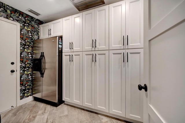 interior space featuring visible vents, white cabinetry, light wood-type flooring, stainless steel fridge, and wallpapered walls