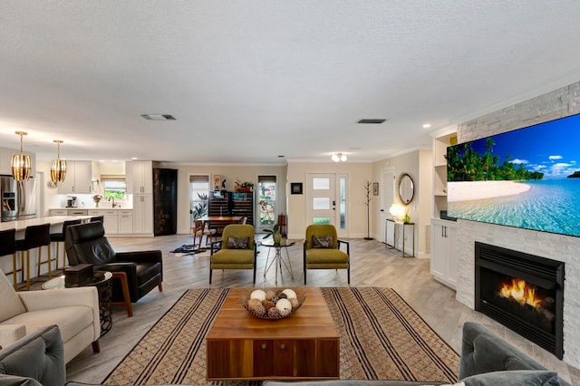 living area with visible vents, ornamental molding, a textured ceiling, light wood-type flooring, and a fireplace