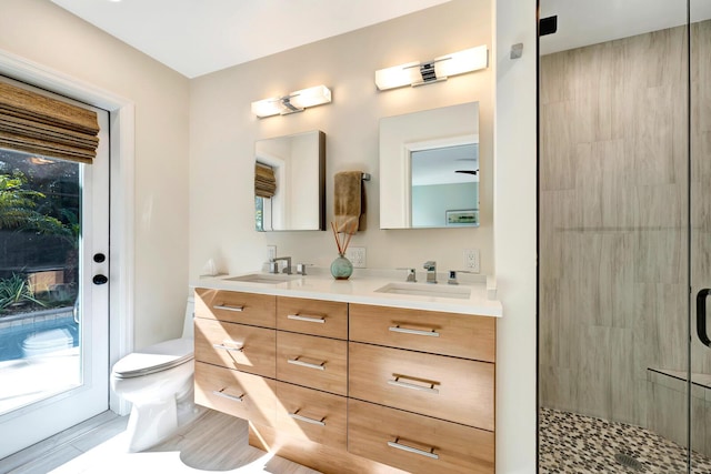 full bathroom featuring double vanity, tiled shower, a sink, and toilet