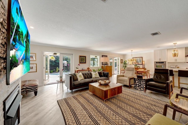 living area with french doors, visible vents, light wood-style floors, ornamental molding, and a textured ceiling