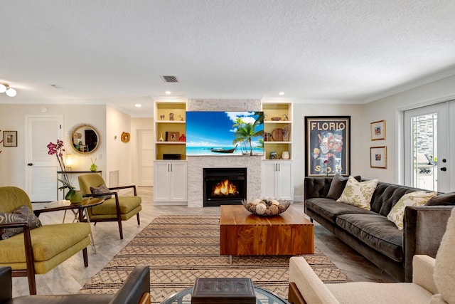 living room featuring a large fireplace, built in features, visible vents, crown molding, and a textured ceiling