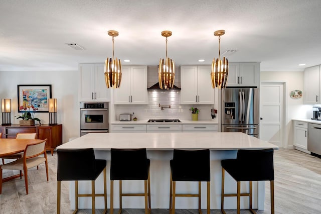 kitchen featuring a kitchen island, appliances with stainless steel finishes, light countertops, wall chimney range hood, and white cabinetry