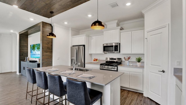 kitchen featuring appliances with stainless steel finishes, white cabinetry, hanging light fixtures, ornamental molding, and a center island with sink