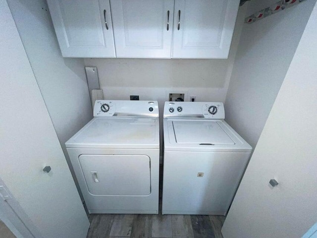 clothes washing area with dark wood-type flooring, washer and clothes dryer, and cabinets