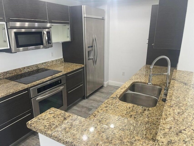 kitchen featuring appliances with stainless steel finishes, sink, light stone counters, and light hardwood / wood-style flooring