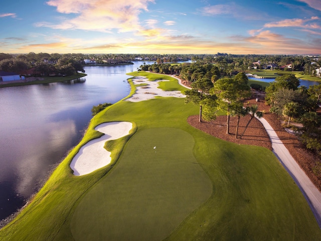 aerial view at dusk featuring view of golf course and a water view