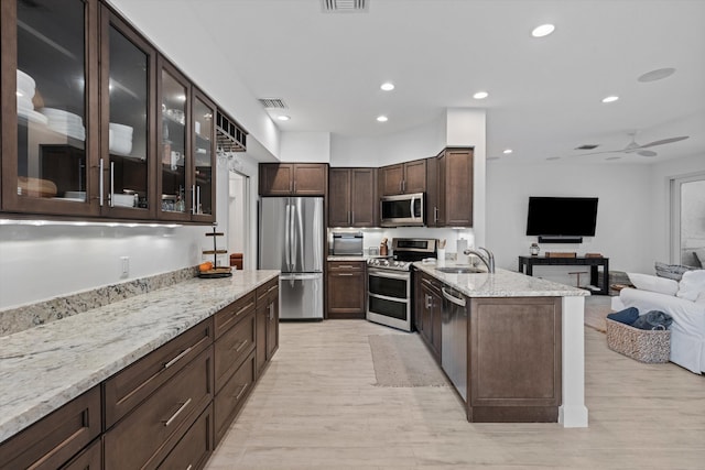 kitchen with visible vents, appliances with stainless steel finishes, glass insert cabinets, open floor plan, and light stone countertops