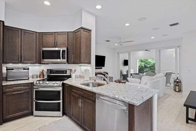 kitchen with a peninsula, appliances with stainless steel finishes, open floor plan, and a sink