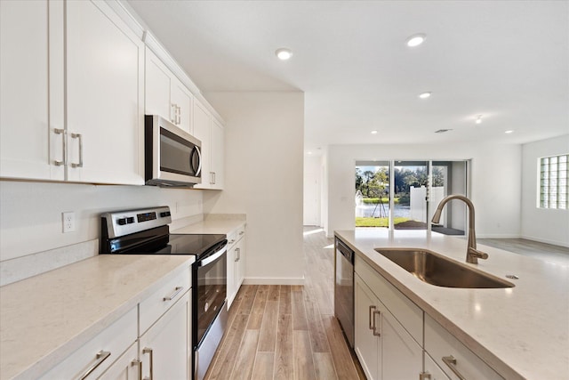 kitchen with light wood finished floors, recessed lighting, white cabinets, stainless steel appliances, and a sink