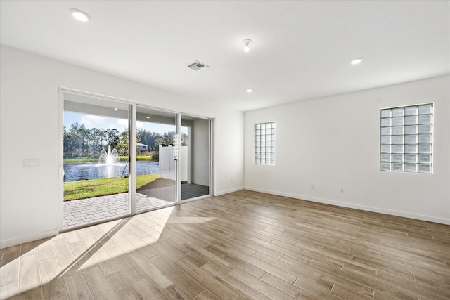 unfurnished room featuring visible vents, baseboards, a water view, recessed lighting, and wood finished floors