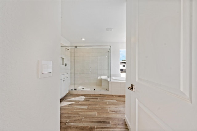 bathroom with wood tiled floor, a stall shower, a tub, recessed lighting, and vanity