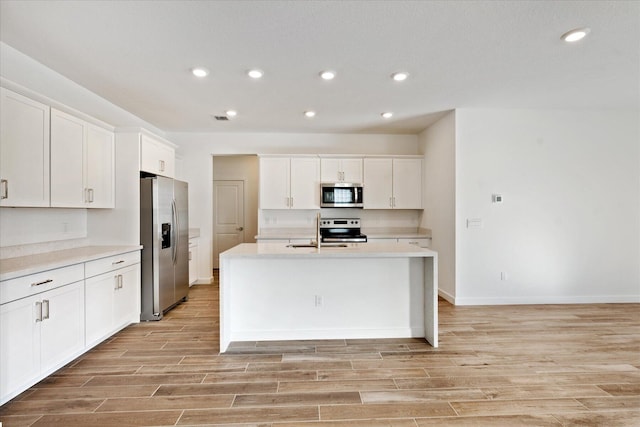 kitchen with a kitchen island with sink, white cabinetry, stainless steel appliances, light wood-style floors, and light countertops