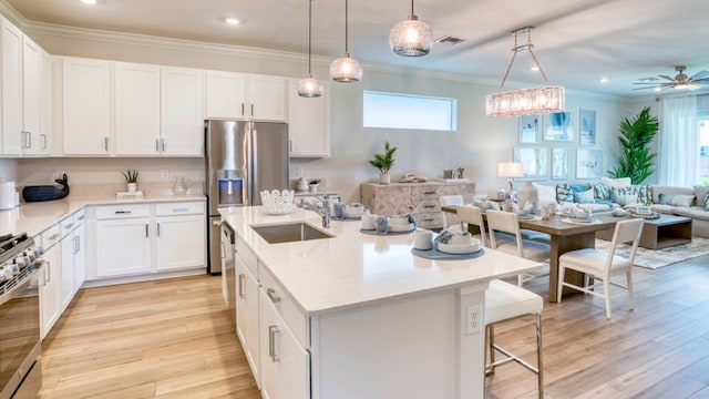 kitchen with ornamental molding, a sink, open floor plan, stainless steel appliances, and light wood-style floors