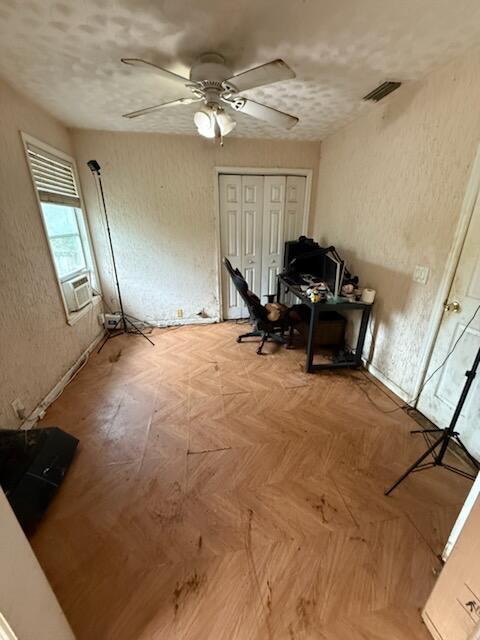 home office with ceiling fan, a textured wall, cooling unit, and visible vents