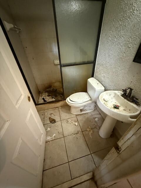 full bathroom featuring a textured wall, toilet, a stall shower, a sink, and tile patterned floors