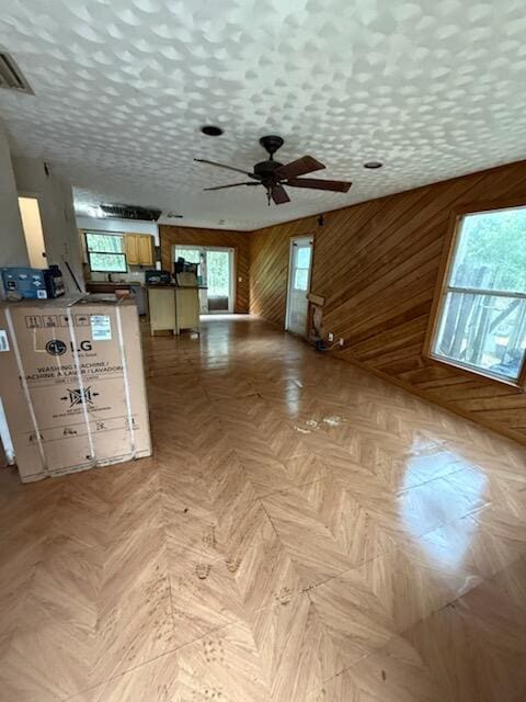 interior space featuring a textured ceiling, ceiling fan, wood walls, and visible vents