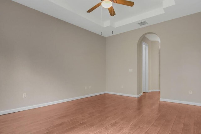6731 Southport Dr W, Boynton Beach, FL 33472 - empty room featuring light wood-style flooring, baseboards, a ceiling fan, arched walkways, and a tray ceiling
