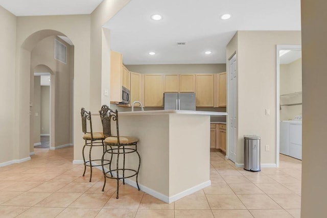 6731 Southport Dr W, Boynton Beach, FL 33472 - kitchen with a peninsula, appliances with stainless steel finishes, light brown cabinets, arched walkways, and light tile patterned floors