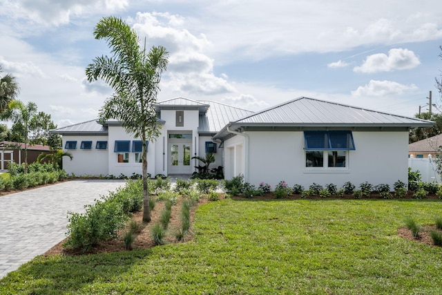 prairie-style house with metal roof, a front lawn, decorative driveway, and stucco siding