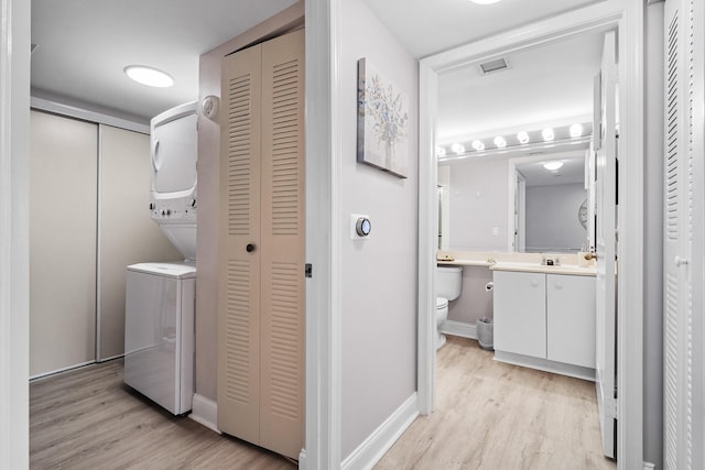 clothes washing area with stacked washing maching and dryer and light hardwood / wood-style floors