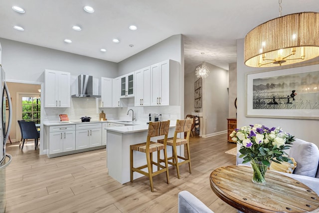 kitchen featuring pendant lighting, sink, white cabinets, wall chimney range hood, and an inviting chandelier