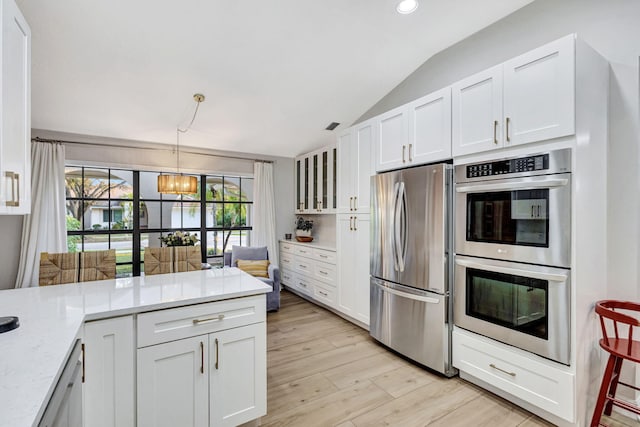 kitchen with stainless steel appliances, vaulted ceiling, hanging light fixtures, and white cabinets