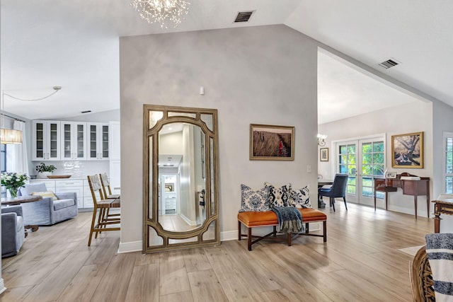 foyer entrance featuring a notable chandelier, high vaulted ceiling, light hardwood / wood-style floors, and french doors