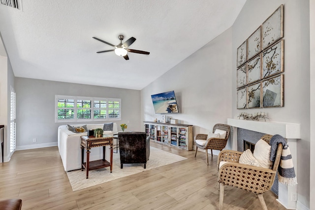 living room with a textured ceiling, vaulted ceiling, light hardwood / wood-style floors, and ceiling fan